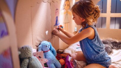 Vue latérale d'une fille dessinant avec du crayon sur le mur d'une maison en carton assise à l'intérieur et s'amusant à la maison.
