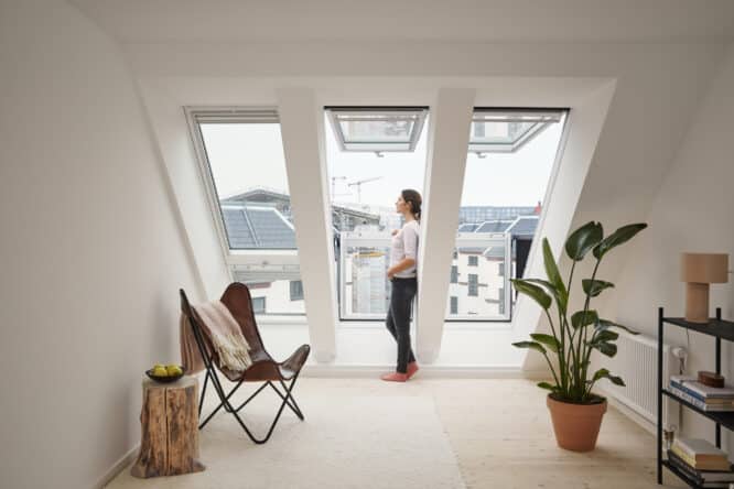 Chambre mansardée avec grandes fenêtres de toit VELUX, vue sur la ville et décoration moderne.