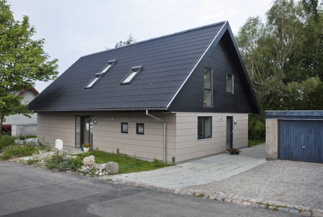 Maison moderne avec toit en tuiles foncées et fenêtres de toit VELUX, jardin et garage.
