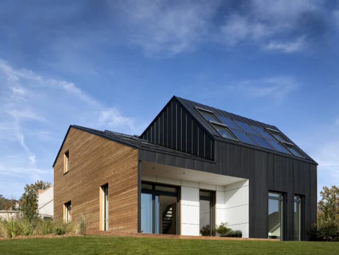 Maison moderne avec toit métallique et fenêtres de toit VELUX, entourée de verdure.