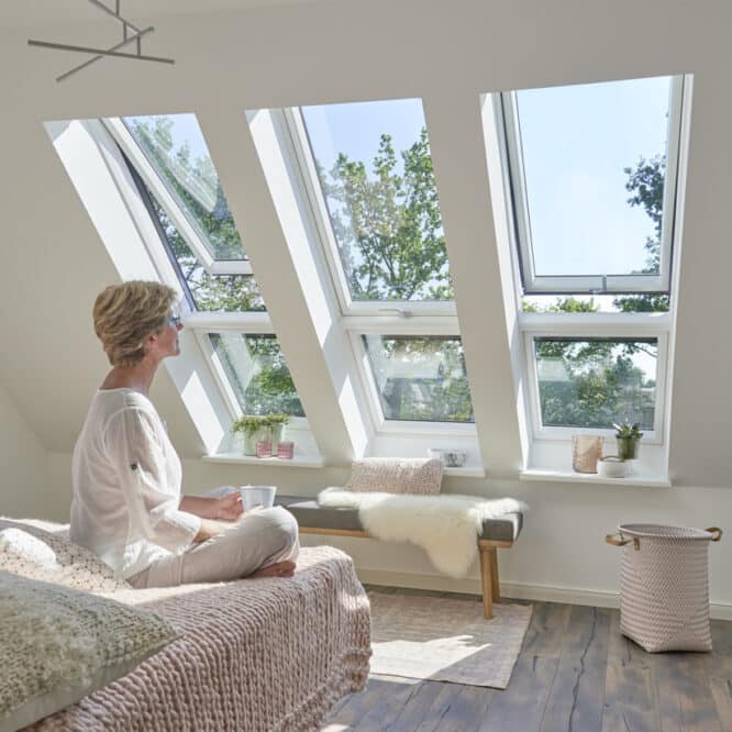 Femme assise sur son lit regardant l'extérieur à travers une combinaison XXL de fenêtres de toit VELUX