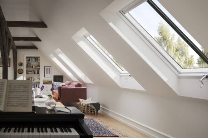 Chambre mansardée avec plafond en pente, fenêtres VELUX, piano et canapé.