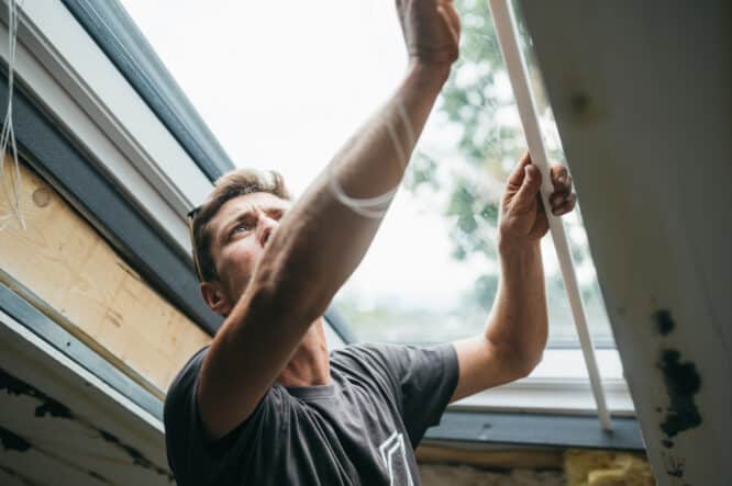 Un homme ajuste une fenêtre de toit VELUX dans une pièce mansardée avec un plafond en pente.