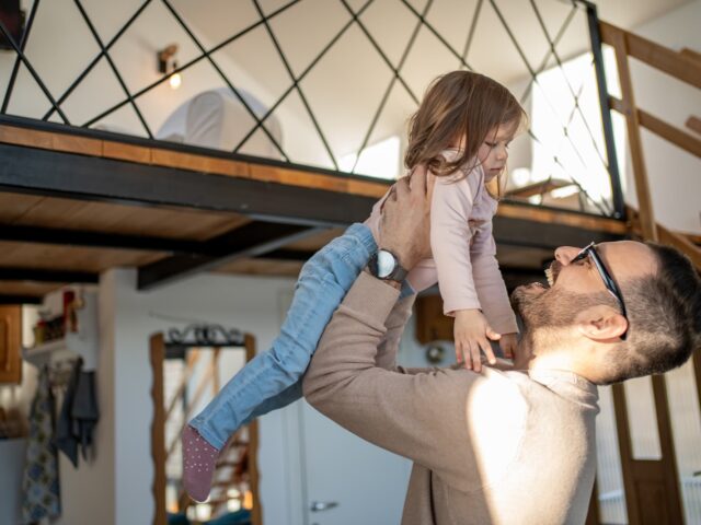 Heureux père soulevant sa fille dans les airs dans leur appartement en duplex, avec une mezzanine