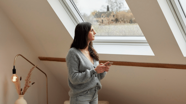 Une jeune femme regarde un ciel pluvieux à travers une fenêtre de toit.