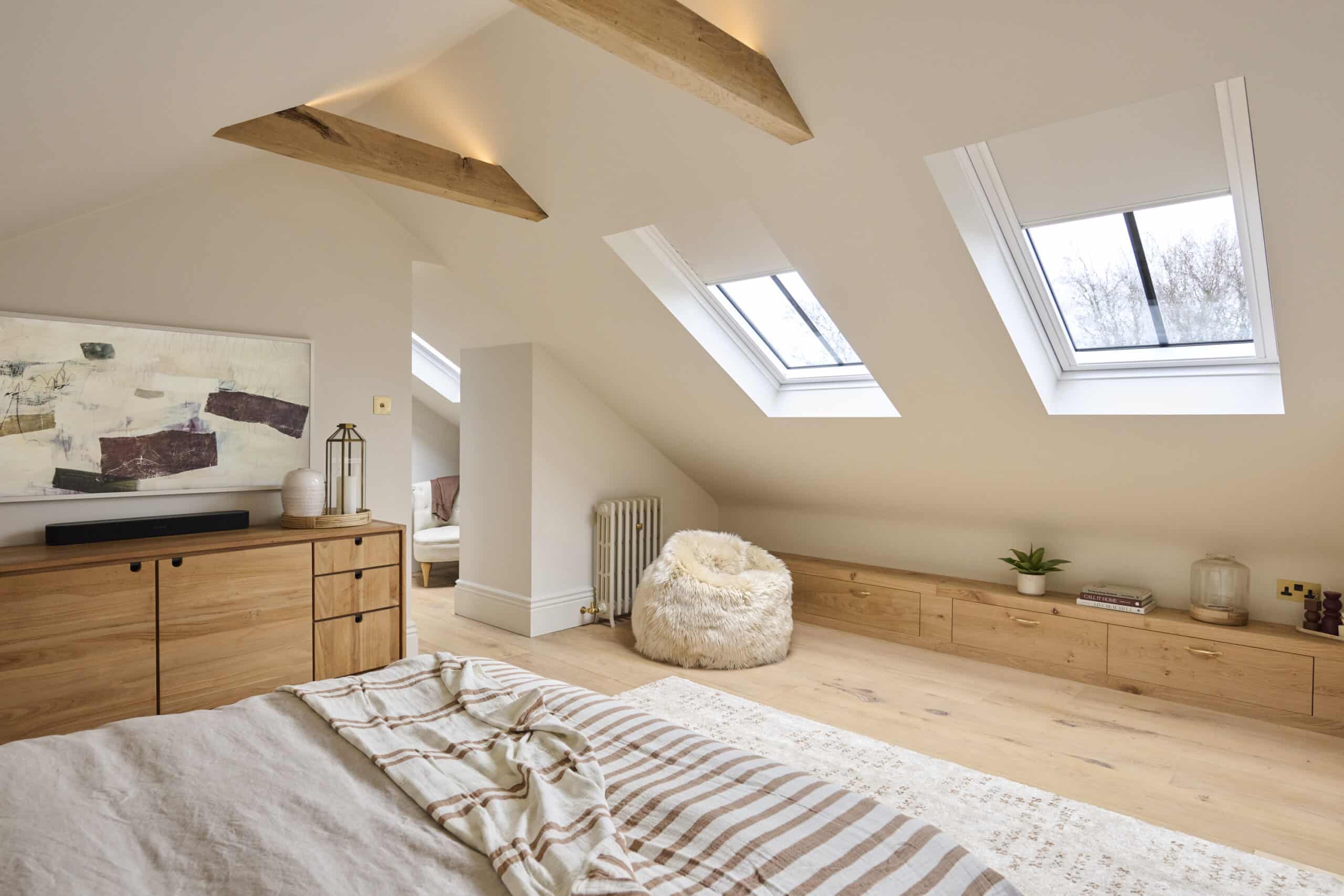 Chambre lumineuse sous les combles avec fen&ecirc;tres de toit VELUX, poutres en bois et rangements int&eacute;gr&eacute;s.