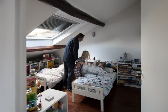 Père couchant ses deux enfants dans une chambre sous combles