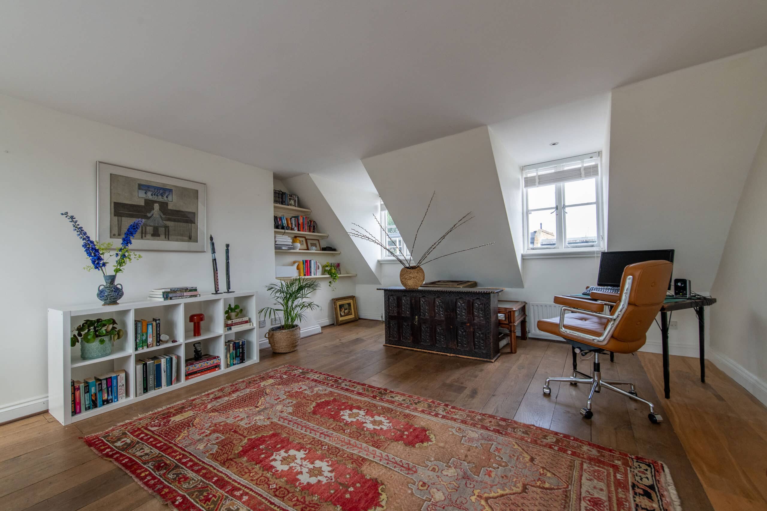 Bureau &agrave; domicile sous les combles avec plafond en pente, fen&ecirc;tre, bureau et &eacute;tag&egrave;res.