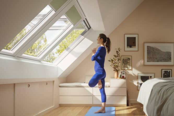 Femme faisant du yoga face aux grandes fenêtres de toit dans sa chambre sous comble