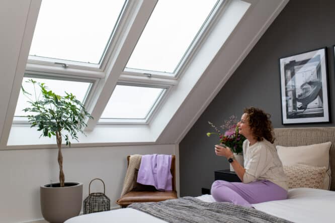 Femme regardant à travers les grandes fenêtres de toit de sa chambre sous combles.