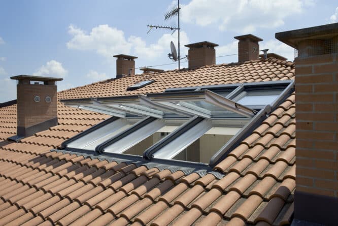 Ouverture les fenêtres de toit VELUX sur un toit en tuiles pour laisser entrer la lumière et l'air à l'intérieur.