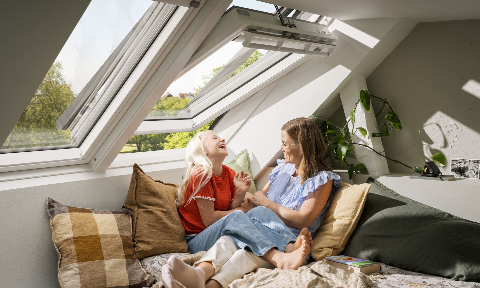 Chambre mansardée avec plafond incliné et fenêtre de toit VELUX ouverte, deux personnes se reposant sur le lit.