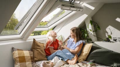 Chambre mansardée avec plafond incliné et fenêtre de toit VELUX ouverte, deux personnes se reposant sur le lit.
