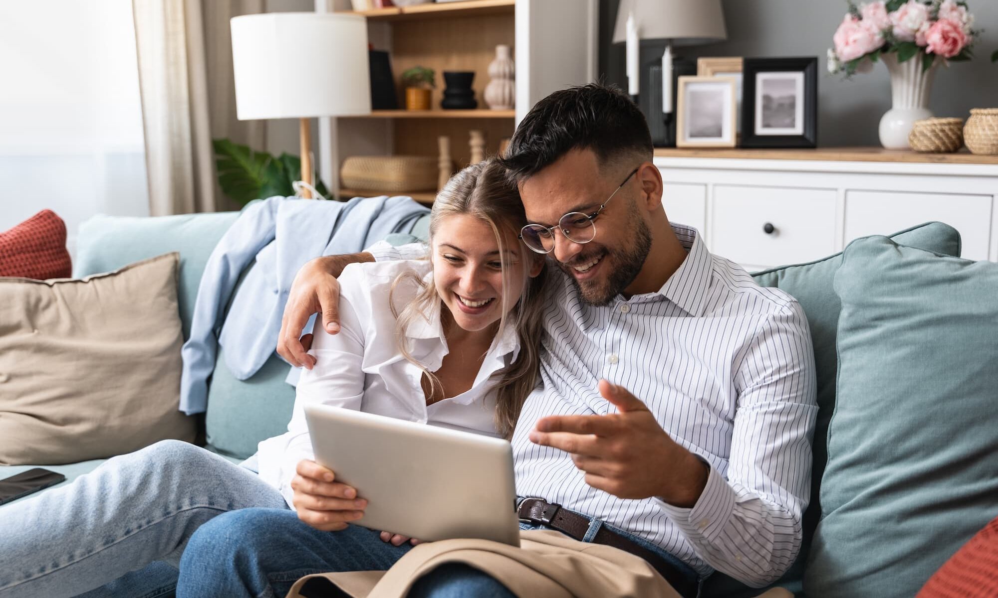 Jeune couple assis sur un canapé avec tablette pour regarder leurs plans d'aménagement.