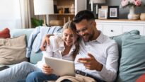 Jeune couple assis sur un canapé avec tablette pour regarder leurs plans d'aménagement.