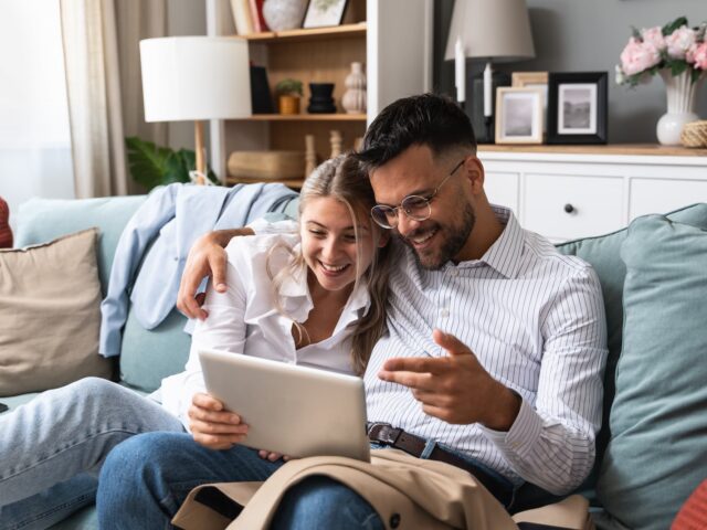 Jeune couple assis sur un canapé avec tablette pour regarder leurs plans d'aménagement.