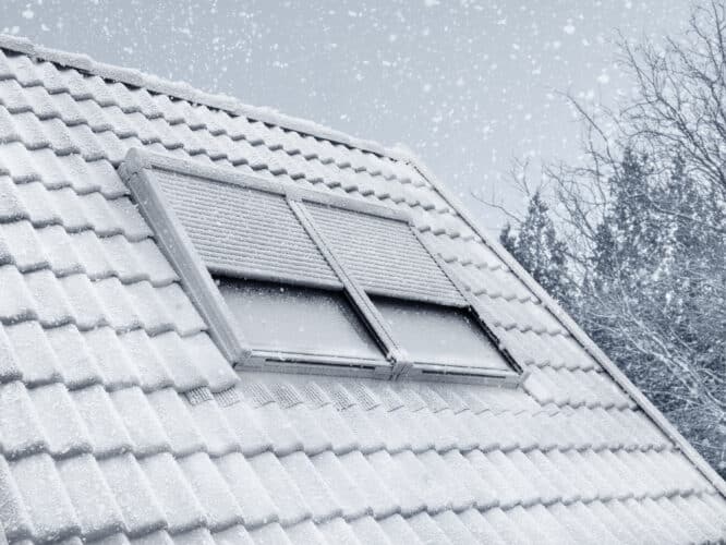 Toiture enneigée avec tuiles, fenêtres de toit VELUX et volets roulants solaires.