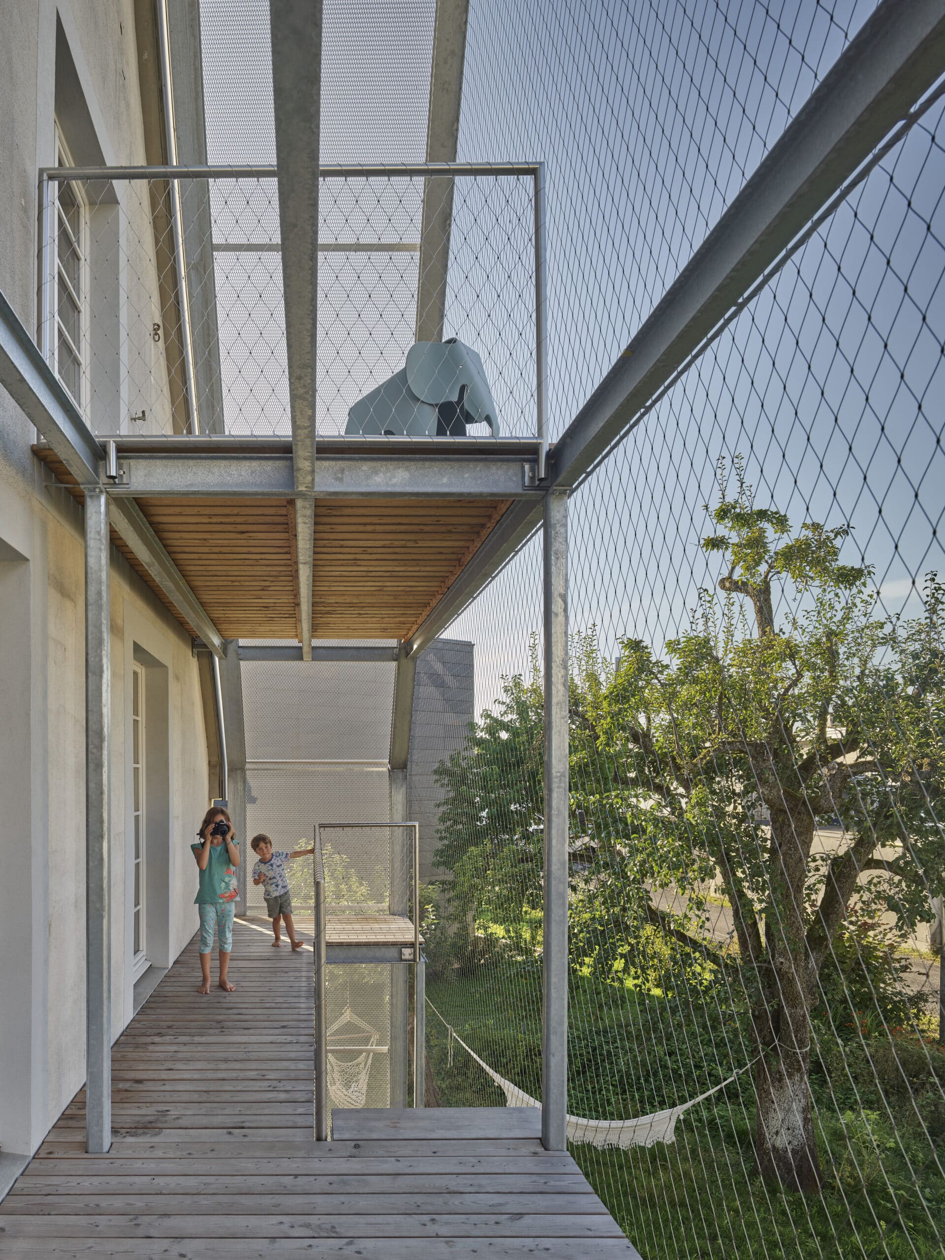 Balcon moderne avec terrasse en bois, rambardes m&eacute;talliques et filet de s&eacute;curit&eacute;.