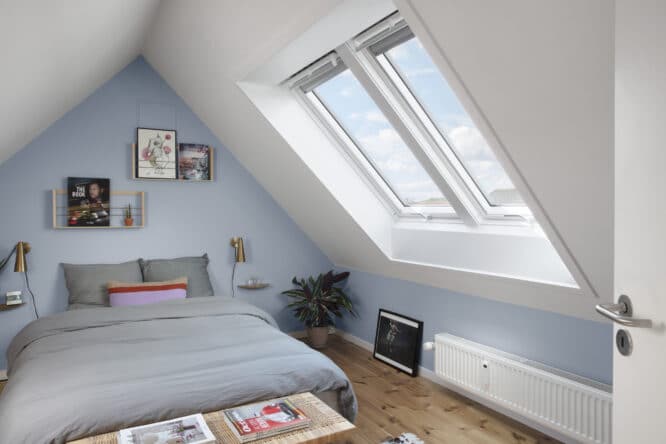 Chambre mansardée avec plafond en pente et fenêtre de toit VELUX, décoration chaleureuse.