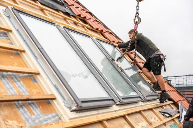 Ouvrier installant des fenêtres de toit VELUX sur un toit en pente avec des chevrons apparents.