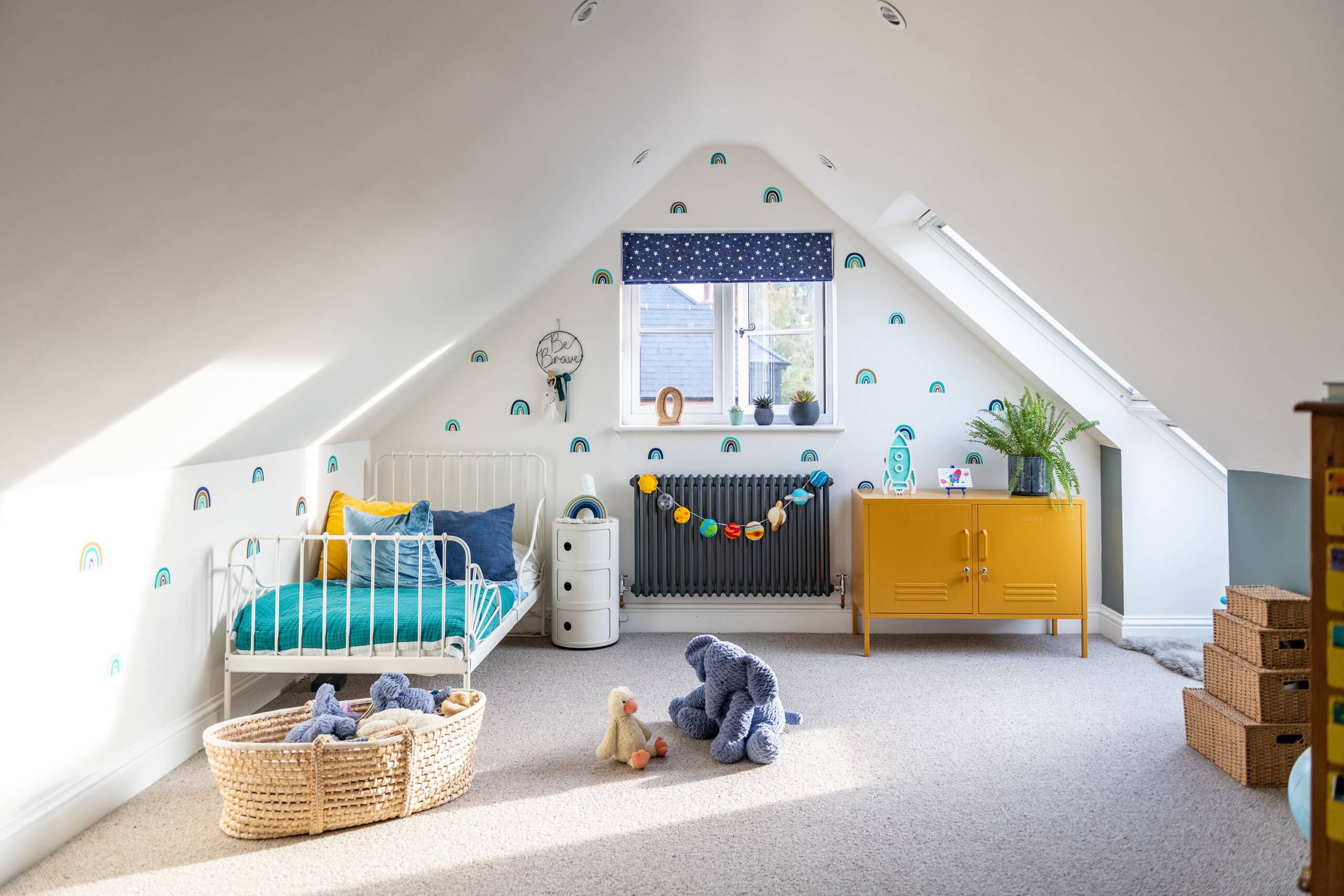 Chambre d'enfant mansard&eacute;e avec plafond en pente, d&eacute;coration arc-en-ciel et fen&ecirc;tre de toit VELUX.