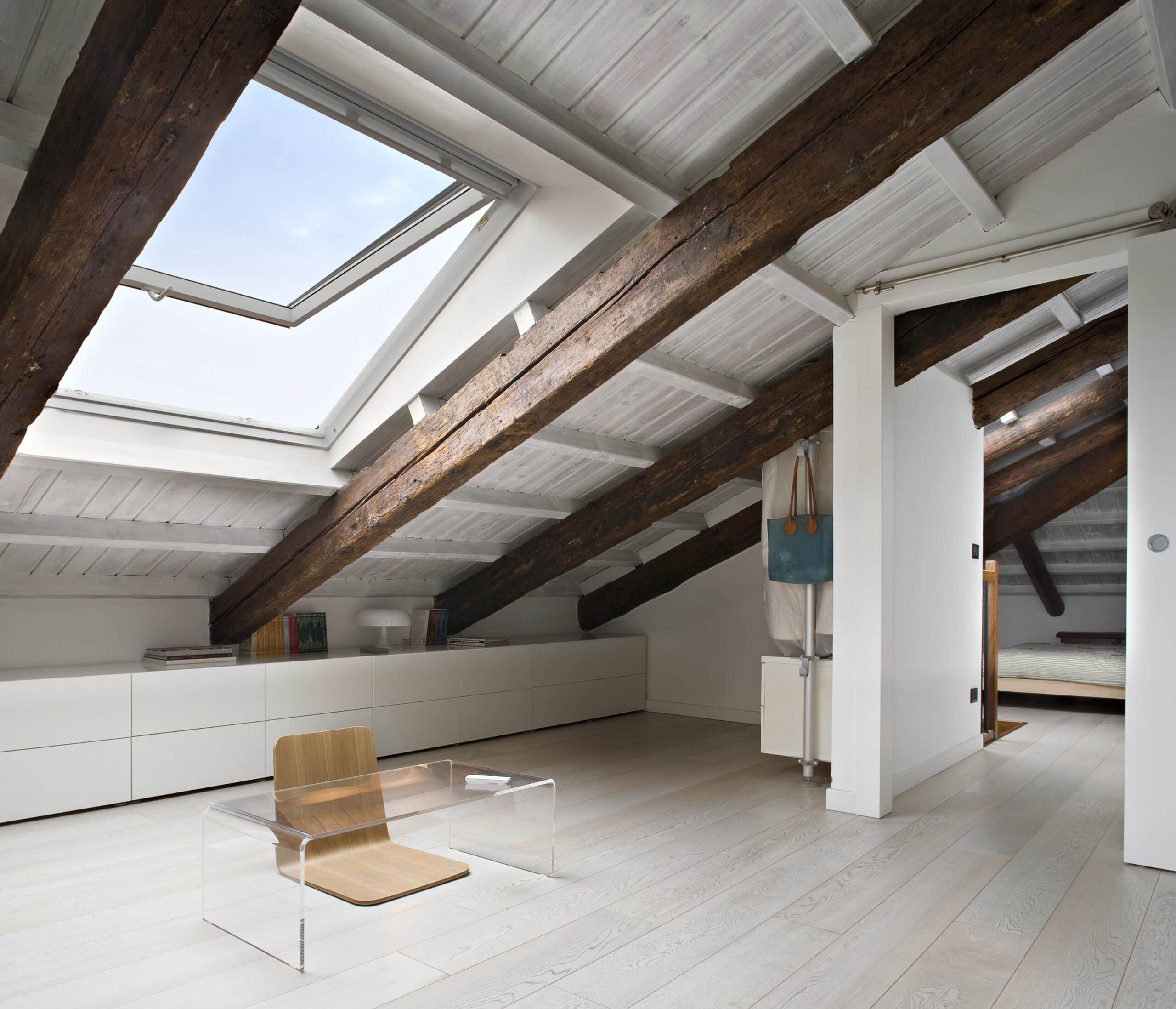 Pi&egrave;ce mansard&eacute;e avec plafond en pente, poutres apparentes et fen&ecirc;tre de toit VELUX ouverte.