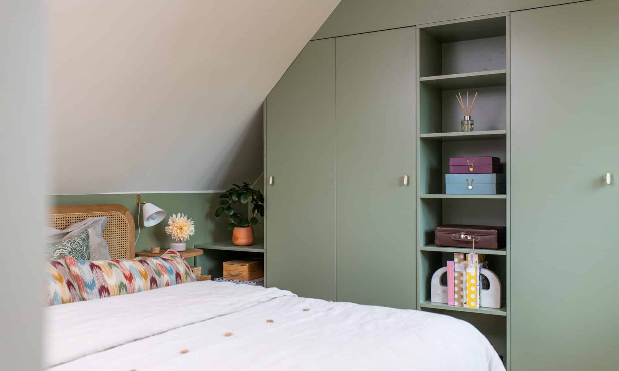 Chambre mansardée avec plafond en pente, décoration verte et armoire intégrée.