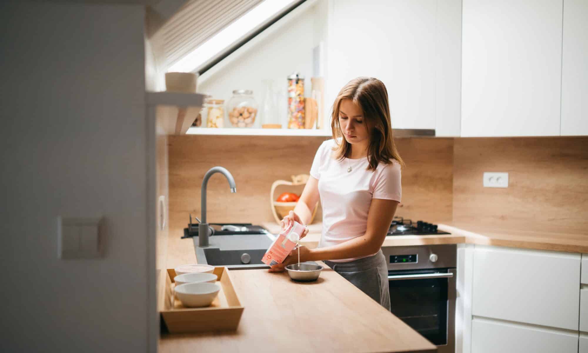 Jeune fille se versant à boire dans une cuisine sous combles.