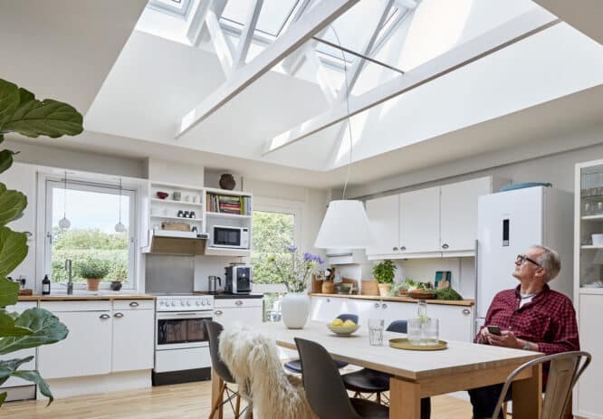Cuisine moderne avec fenêtres de toit VELUX, armoires blanches et table à manger en bois.