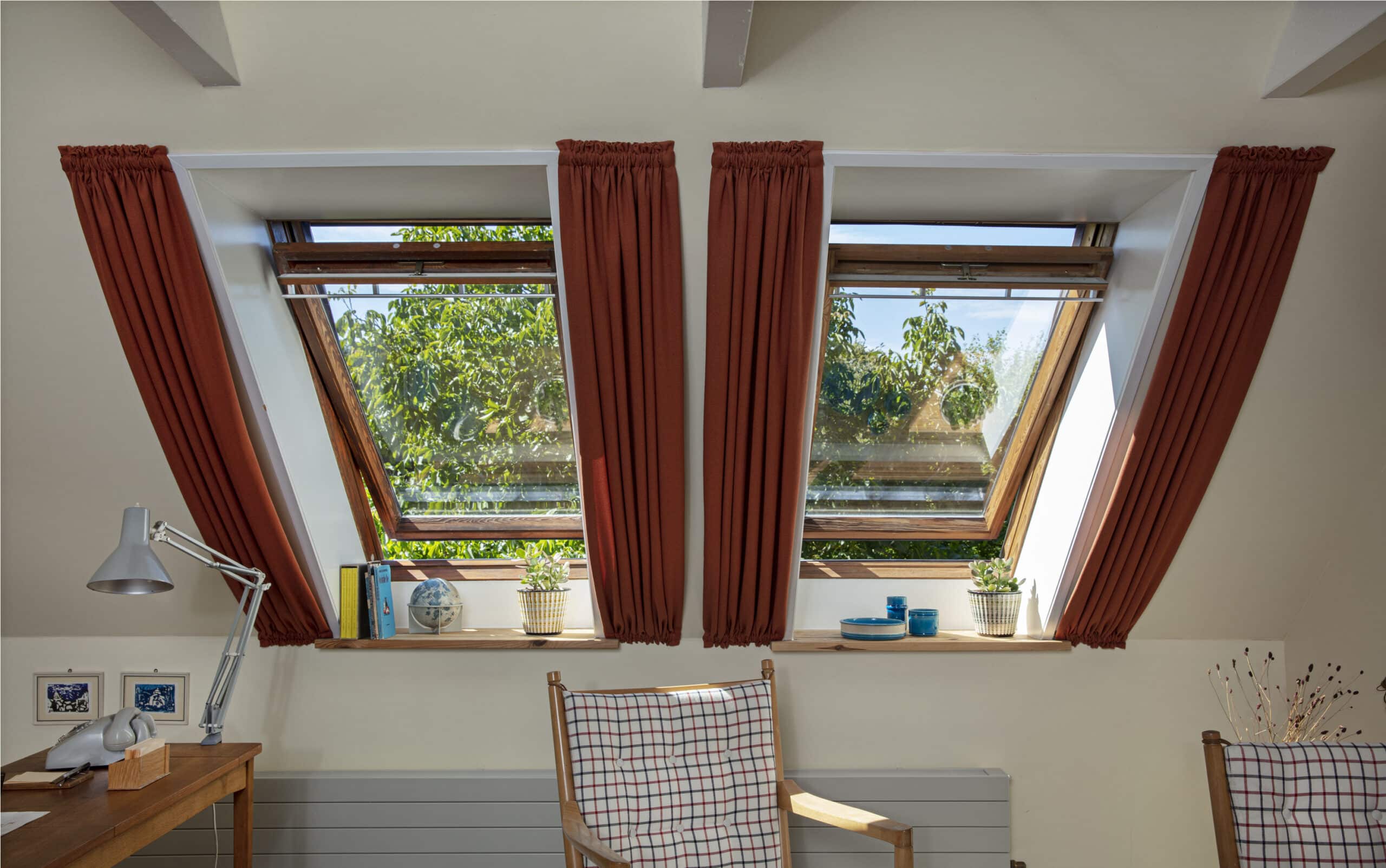 Chambre sous les combles avec fen&ecirc;tres de toit VELUX et rideaux en pente, lumi&egrave;re naturelle et d&eacute;coration chaleureuse.