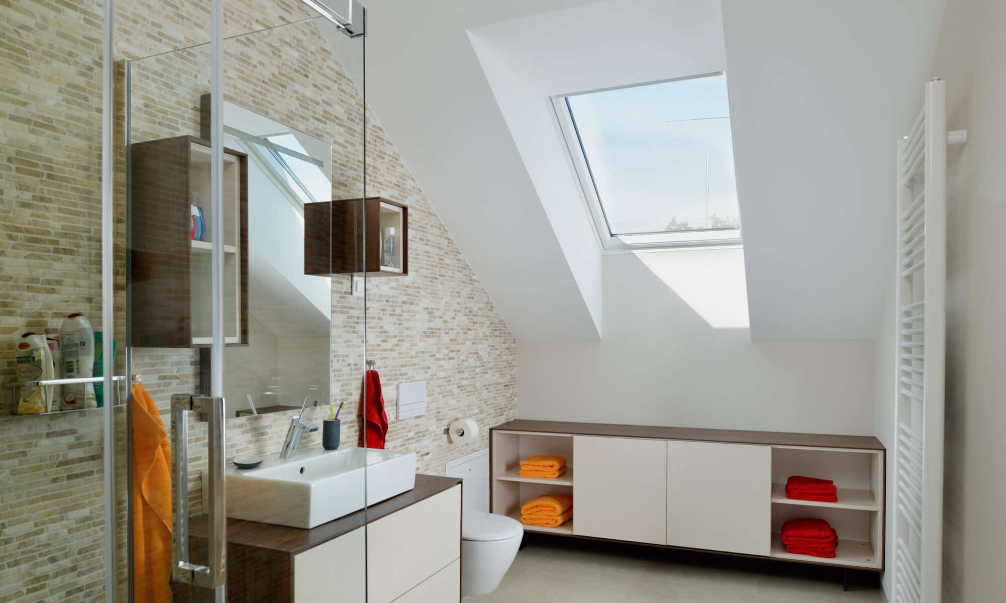 Salle de bains avec plafond mansardé et fenêtre de toit VELUX, équipements modernes.