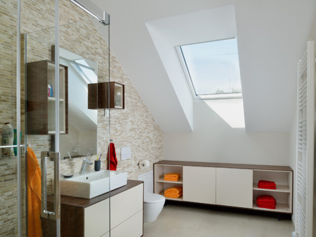 Salle de bains avec plafond mansardé et fenêtre de toit VELUX, équipements modernes.