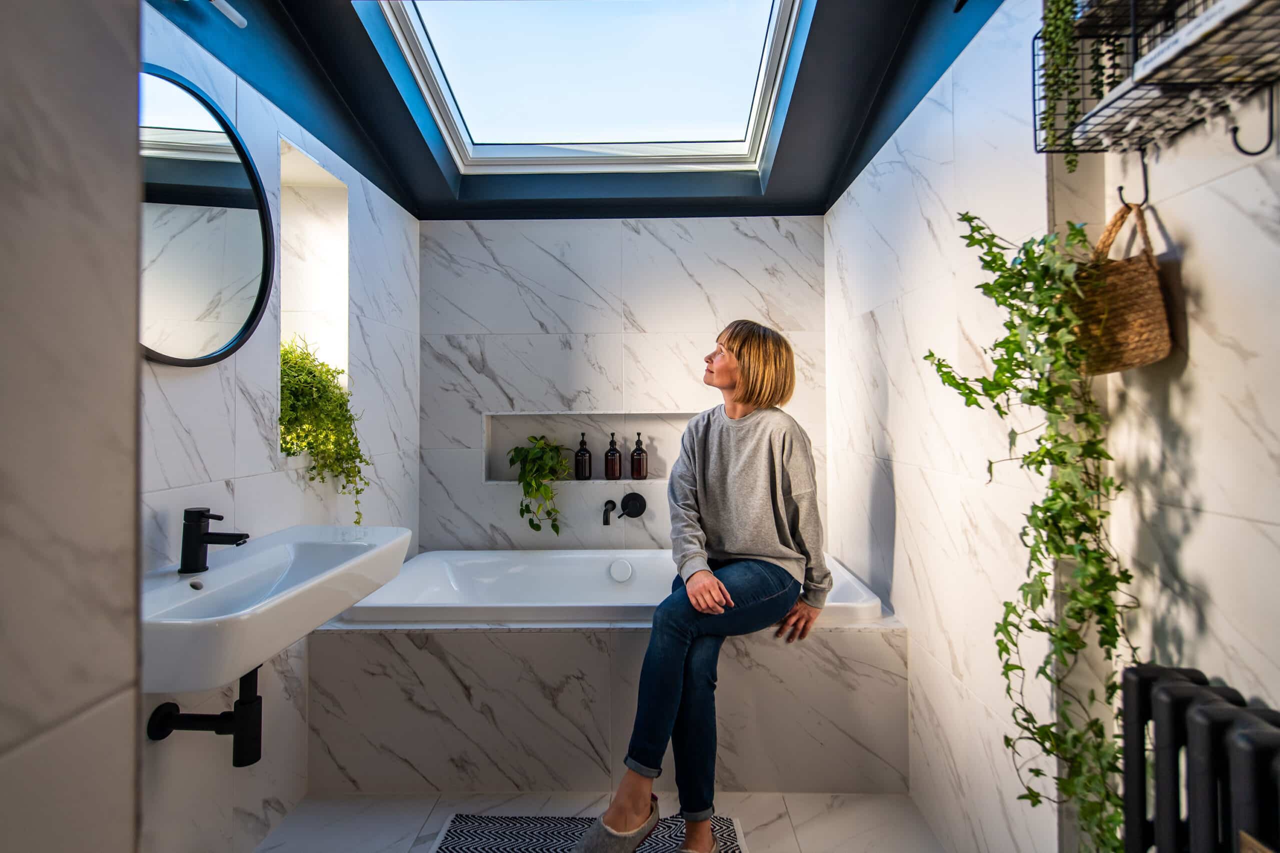 Salle de bains avec carrelage en marbre et fen&ecirc;tre de toit VELUX, laissant entrer la lumi&egrave;re naturelle.