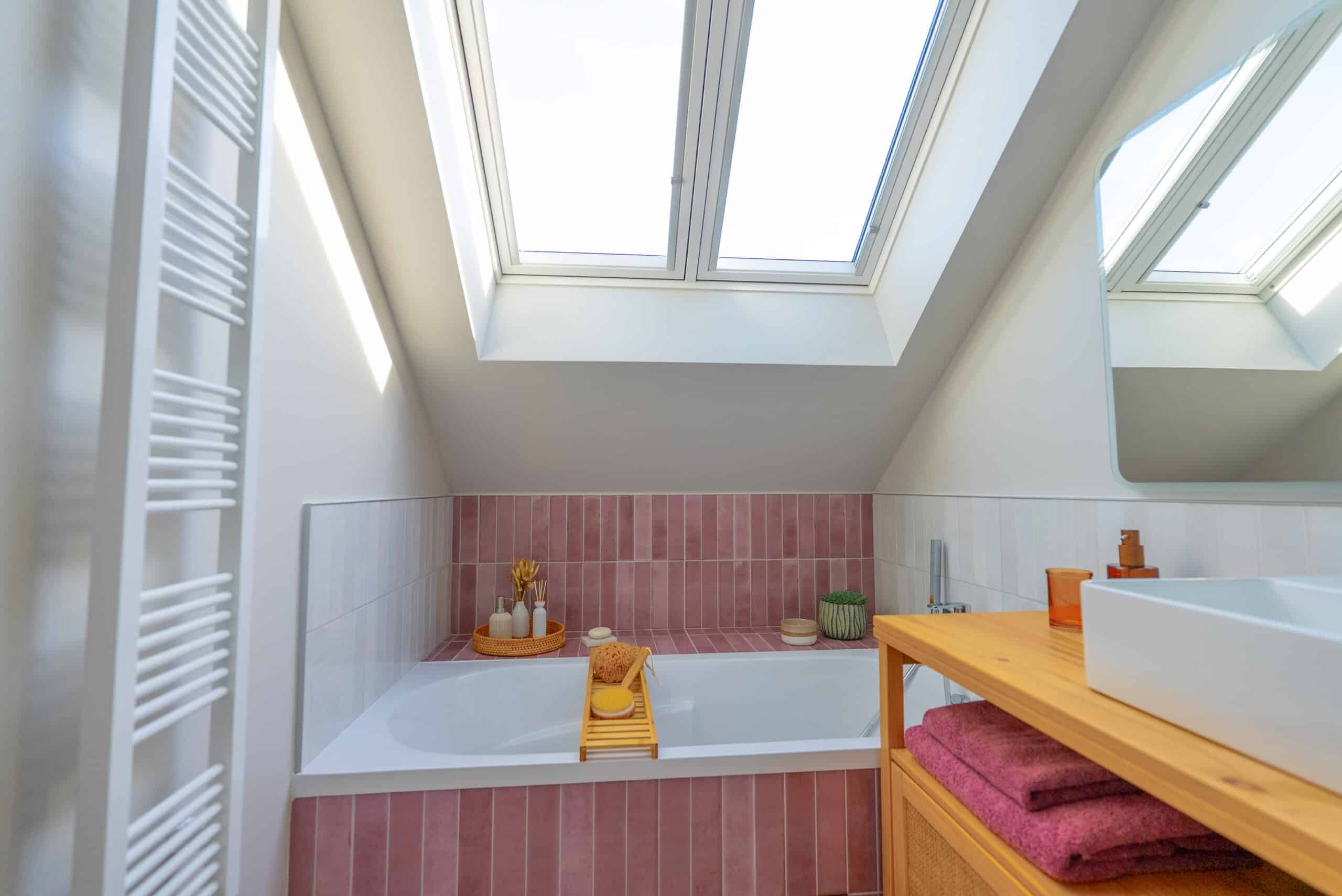 Salle de bains mansard&eacute;e avec fen&ecirc;tre de toit VELUX et carrelage rose.