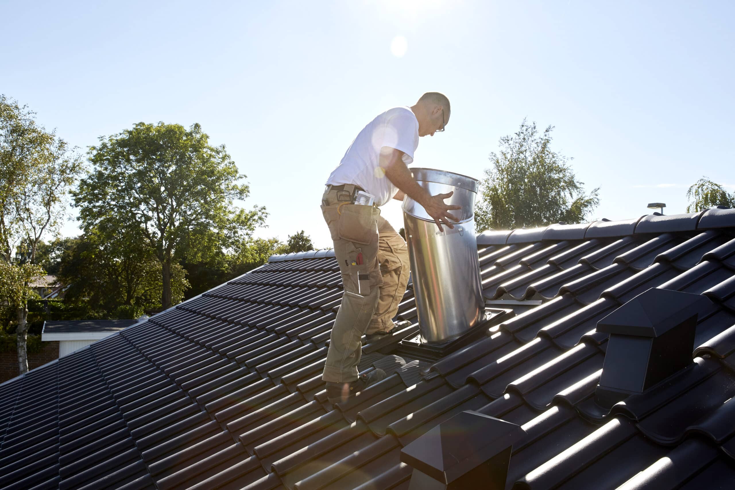 Ouvrier installant un conduit de lumi&egrave;re Sun tunnel VELUX sur un toit en tuiles.