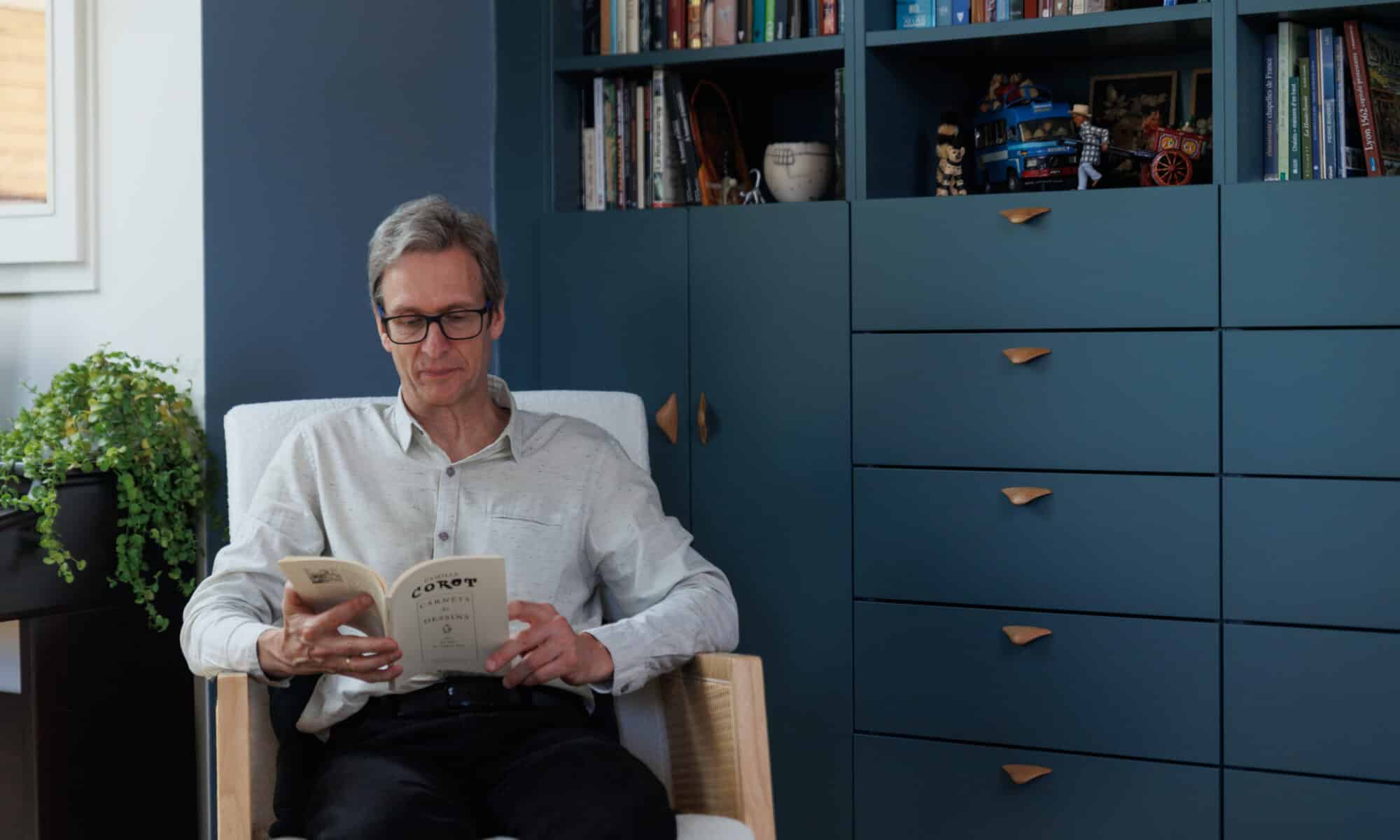 Homme lisant un livre devant une bibliothèque sur mesure dans un appartement sous combles.