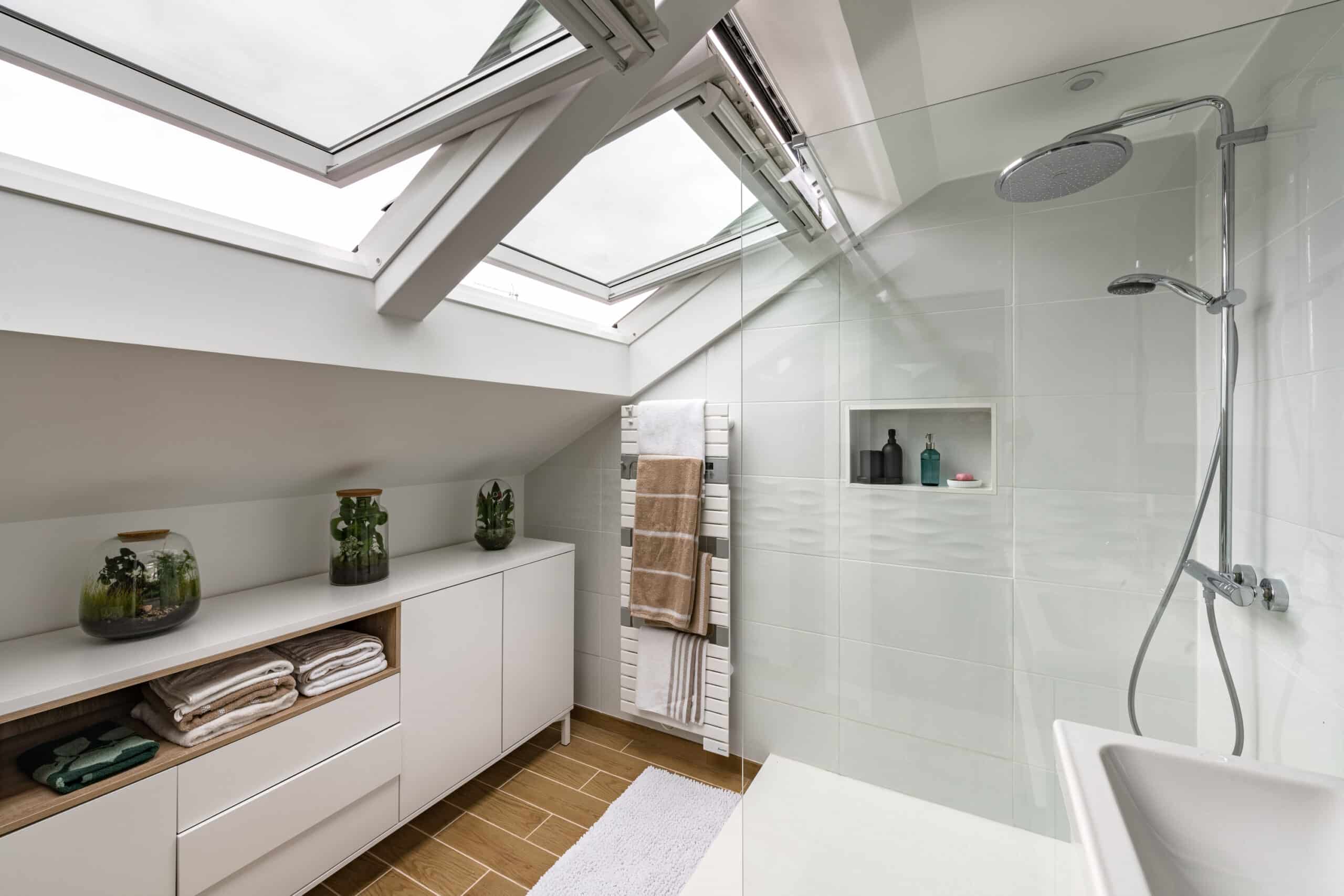 Salle de bains sous combles avec plafond en pente et fenêtre de toit VELUX, au design moderne.