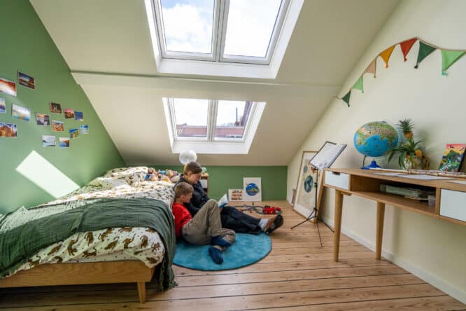 Chambre d'enfants mansardée avec plafond en pente et grandes fenêtres de toit, décoration colorée.
