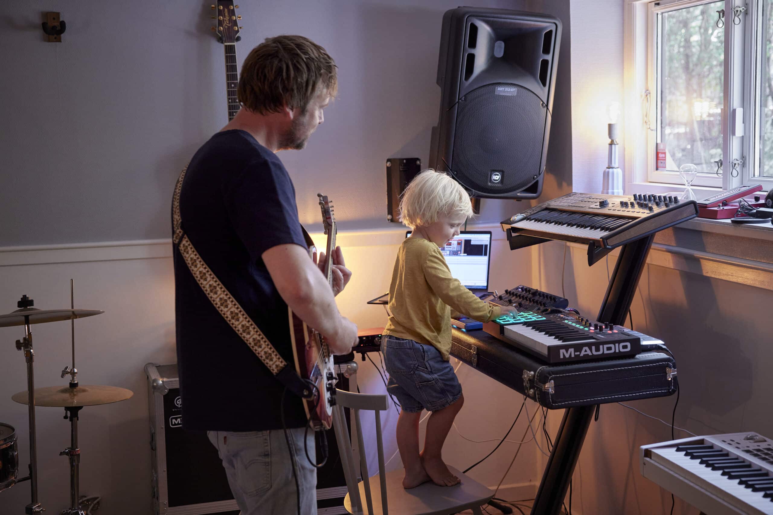 Un père et son enfant dans un studio à domicile, jouant de la guitare et du clavier.