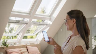 Chambre mansardée avec fenêtres de toit VELUX ouvertes, lumière naturelle et vue sur la verdure.