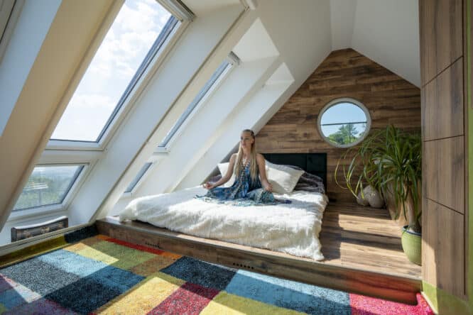 Chambre mansardée avec plafond en pente, fenêtres de toit VELUX, tapis coloré et parquet.