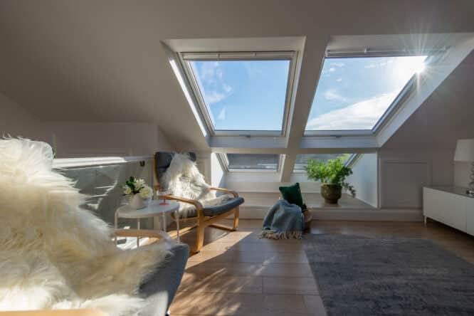 Chambre mansardée avec fenêtres de toit VELUX, sièges confortables et lumière naturelle.