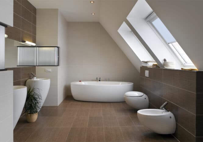 Salle de bain mansardée avec plafond en pente et fenêtres de toit VELUX, équipements modernes.