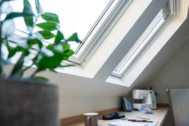 Espace de travail mansardé avec fenêtres de toit VELUX, machine à coudre et papeterie.