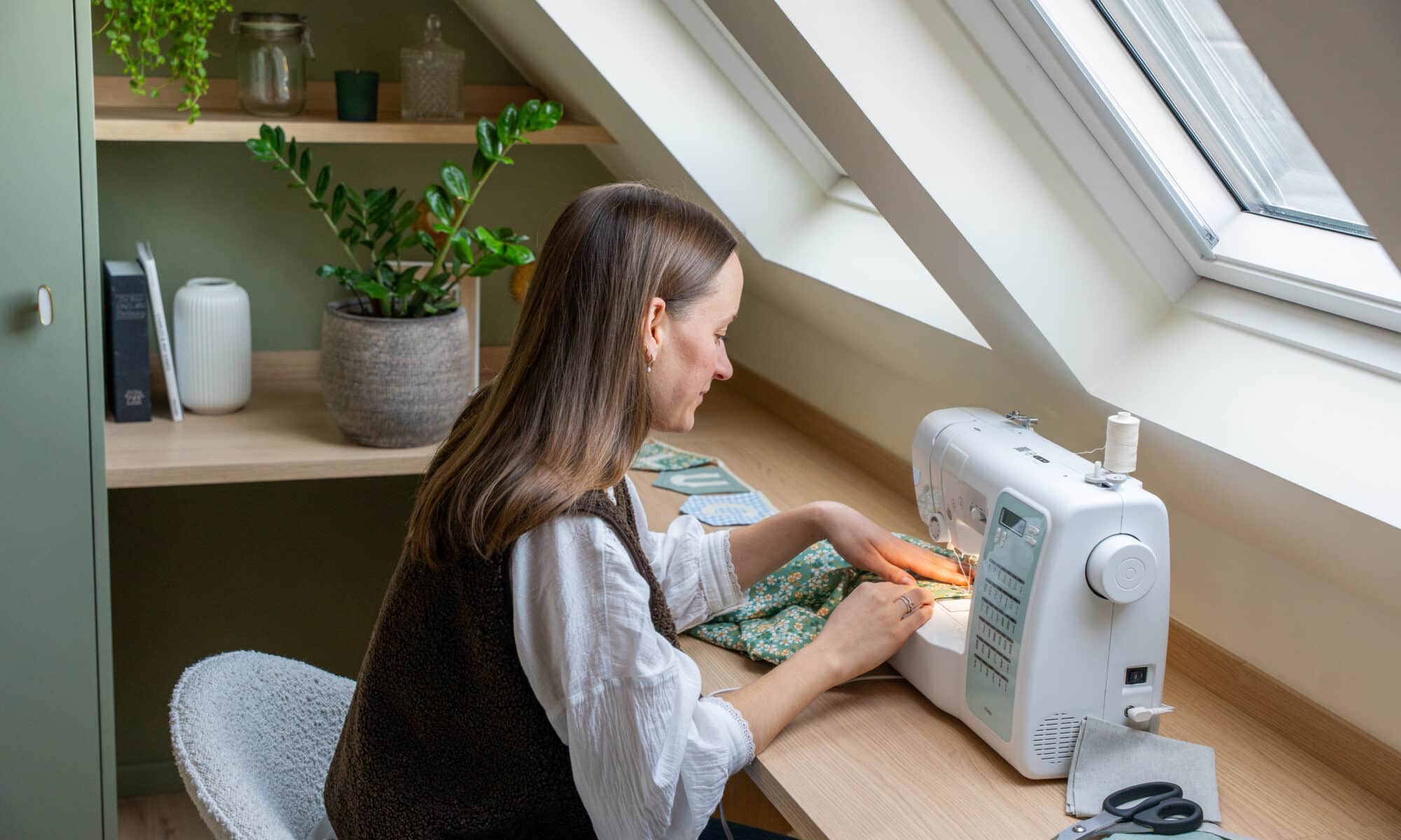 Atelier de couture mansardé avec plafond incliné et fenêtre de toit VELUX, machine à coudre sur le bureau.