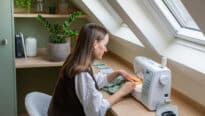 Atelier de couture mansardé avec plafond incliné et fenêtre de toit VELUX, machine à coudre sur le bureau.