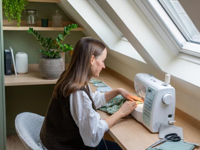 Atelier de couture mansardé avec plafond incliné et fenêtre de toit VELUX, machine à coudre sur le bureau.