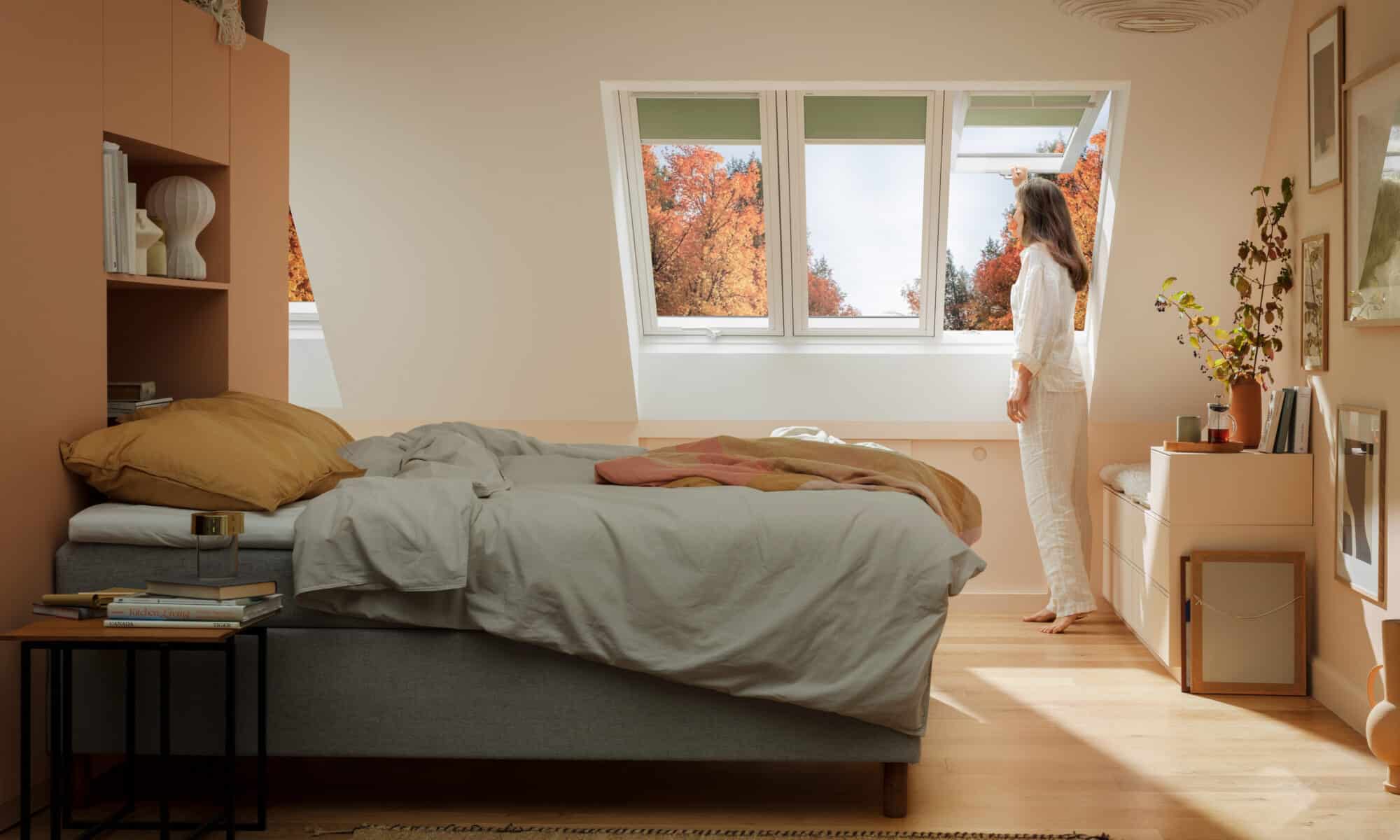 Chambre mansardée avec plafond incliné et fenêtre de toit VELUX, femme admirant la vue.