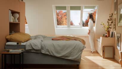 Chambre mansardée avec plafond incliné et fenêtre de toit VELUX, femme admirant la vue.