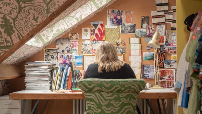 Espace de travail mansardé avec plafond en pente, bureau et tableau en liège rempli de matériel créatif.